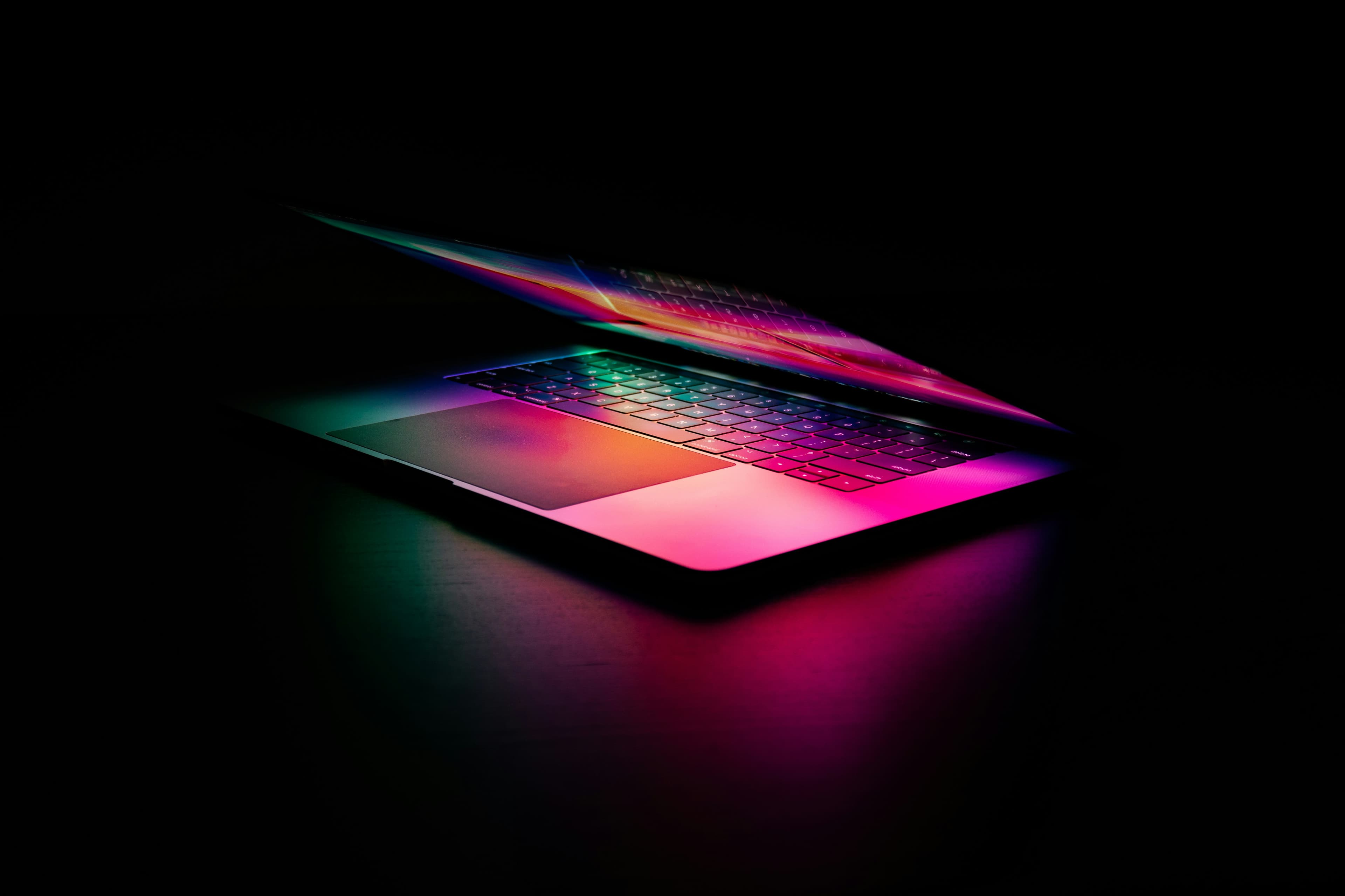 A glowing laptop opens to multicolor pink on a dark background